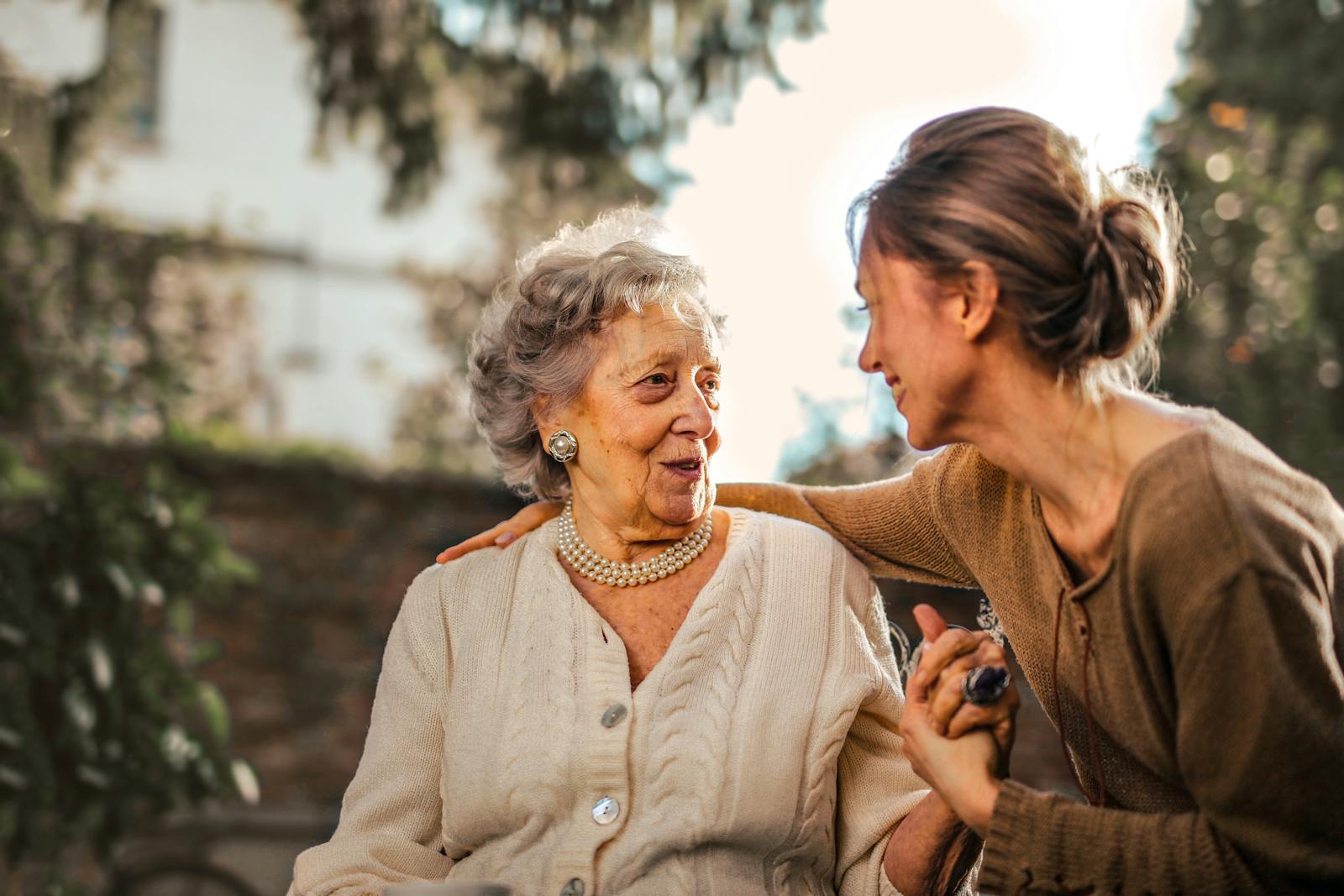 Senior woman smiling warmly with a companion holding her hand in a sunlit garden